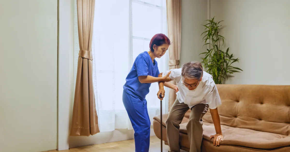 Nurse assisting an elderly man with balance problems in elderly while standing up at home.