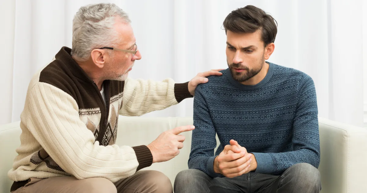 An elderly man in a sweater is consoling a younger man, who appears distressed, symbolizing the emotional and communicative challenges faced by individuals with neurological disorders.