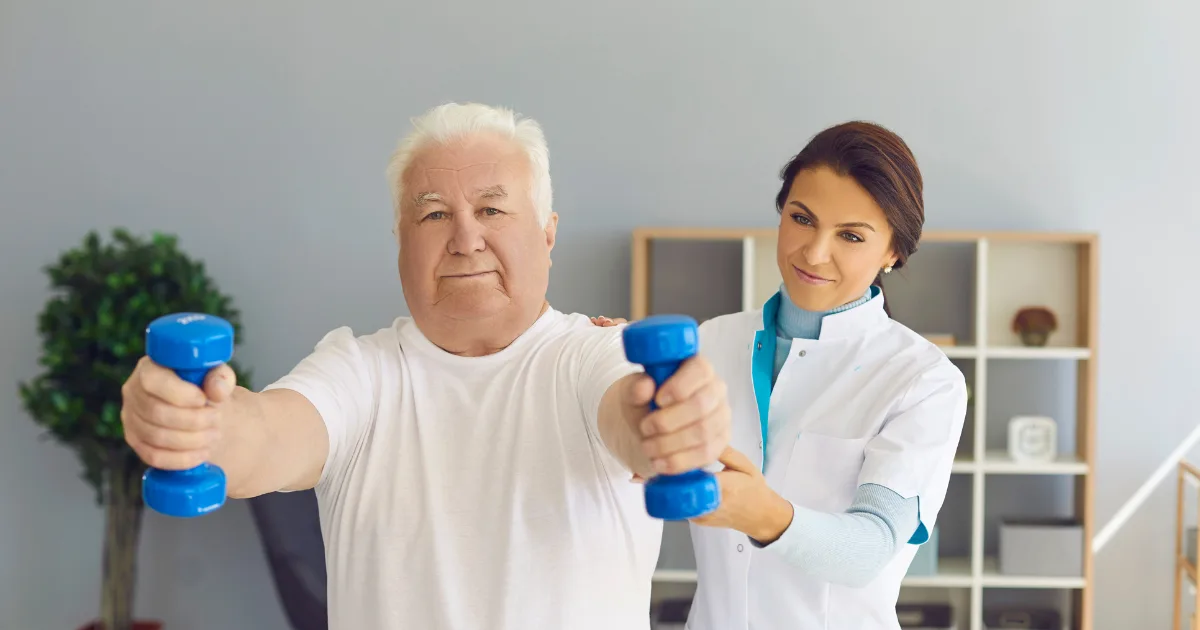 Elderly man receiving occupational therapy, performing arm exercises with dumbbells under therapist supervision.