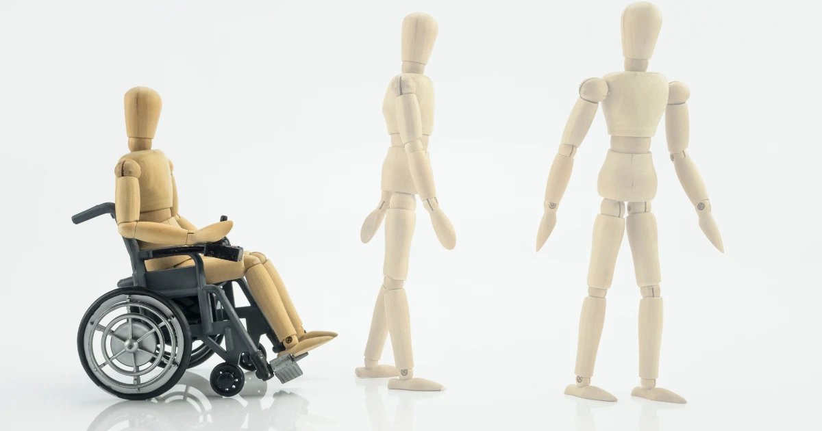 Three wooden mannequins illustrate stages of mobility; one mannequin sits in a wheelchair, while the other two are standing and walking, symbolizing the progression and impact of Multiple System Atrophy on movement.