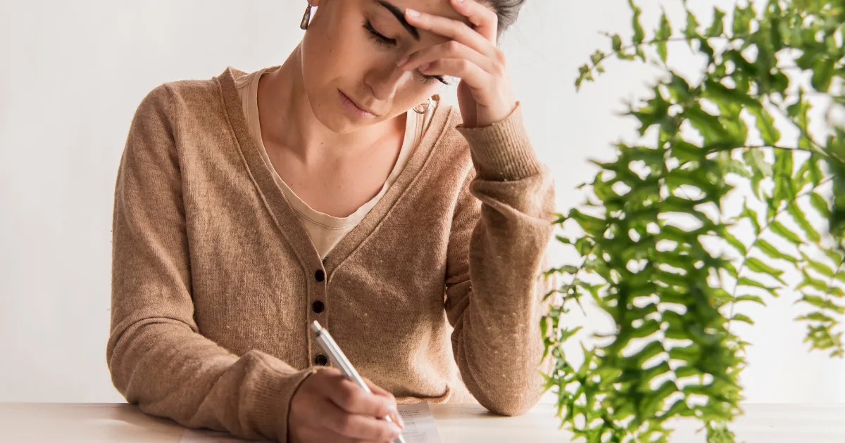 A person appears deep in thought and slightly fatigued while writing at a desk, suggesting the challenges faced during bradykinesia treatment.