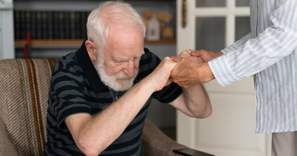 Elderly man experiencing muscle rigidity in Parkinson’s disease receiving support from a caregiver Dr. Mitesh Chandarana