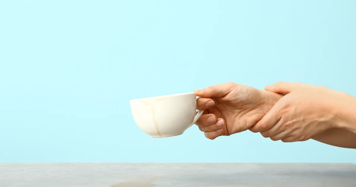 Close-up of a person holding a trembling hand while lifting a coffee cup, representing the link between caffeine and Parkinson’s disease.