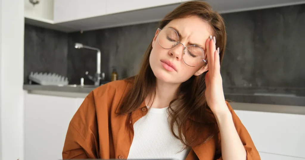 Woman experiencing neurological fatigue, holding her head in discomfort at home.