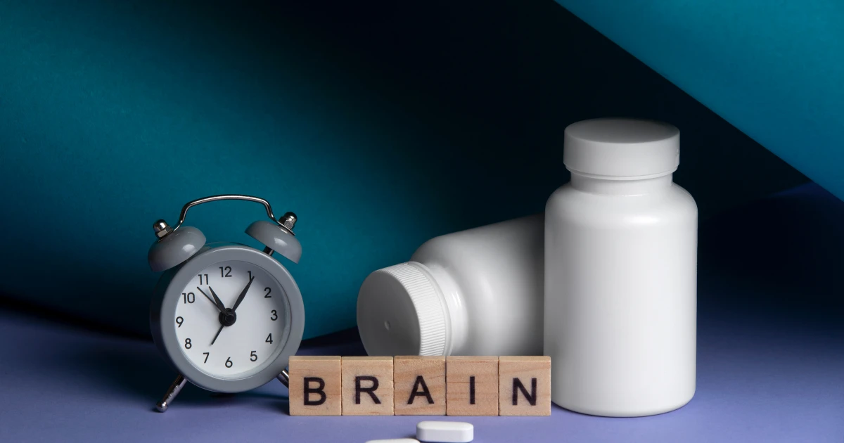 Pills, supplement bottles, a clock, and wooden blocks spelling "BRAIN" arranged together, representing supplements for brain function.