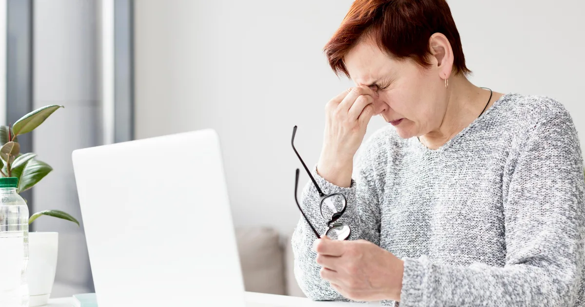 Middle-aged woman rubbing her eyes in front of a laptop, appearing tired and stressed, representing causes of chronic fatigue.