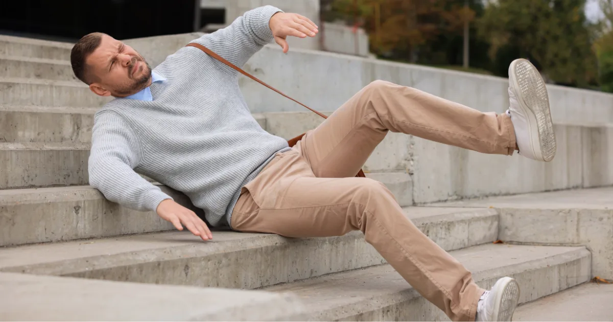 Man losing balance and falling on concrete stairs, representing the risks of frequent falling.