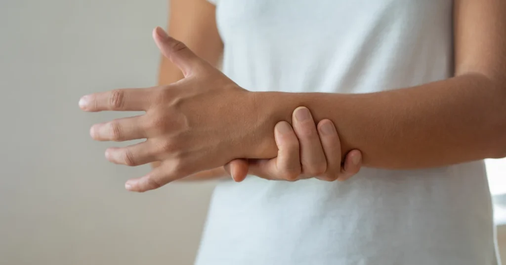 Person holding their wrist to control abnormal hand movement, illustrating symptoms linked to alien limb syndrome.