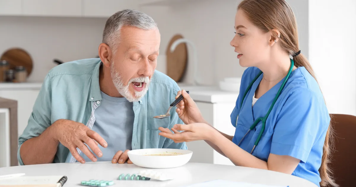 Nurse assisting an elderly man with feeding, representing mobility and coordination challenges seen in PSP vs Parkinson’s.