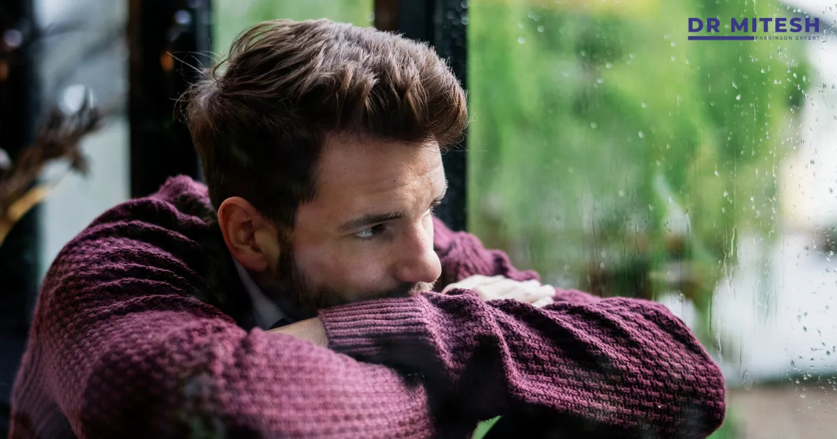 Man sitting by a window looking thoughtful and withdrawn, reflecting emotional distress and feeling sad for a prolonged period.
