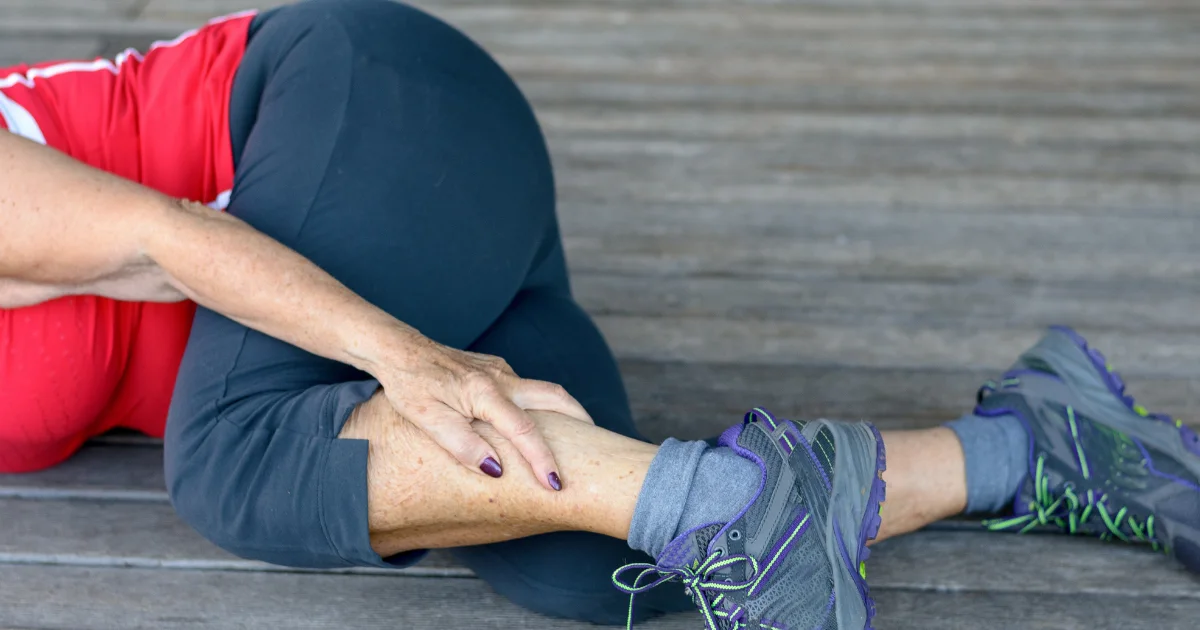 Person holding their lower leg in discomfort while stretching, showing symptoms commonly linked to leg cramps.