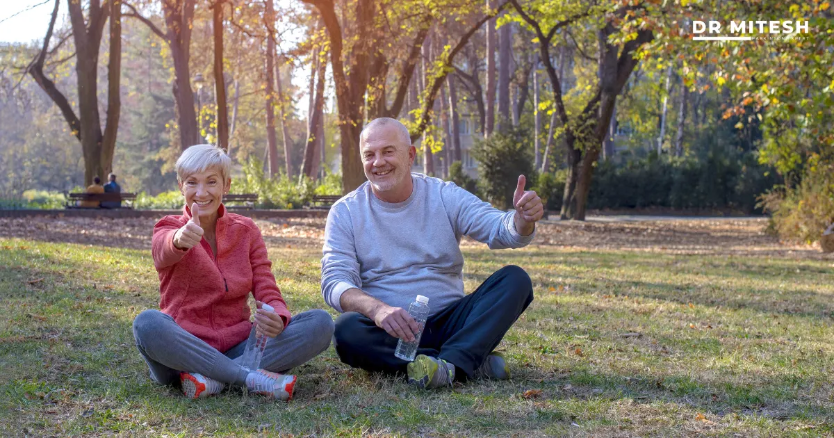 Older couple sitting in a park giving thumbs up, representing return to normal life after recovery from Functional Movement Disorder.