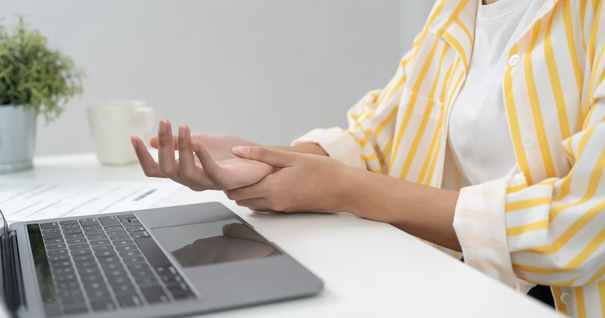 Person holding their wrist in discomfort while working on a laptop, showing symptoms similar to RLS in arms.