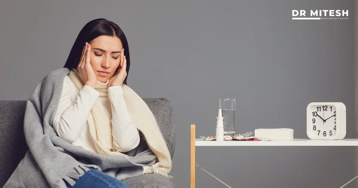 Woman holding her head while sitting on a sofa with medicines nearby, representing medicine side effect from long-term drug use.